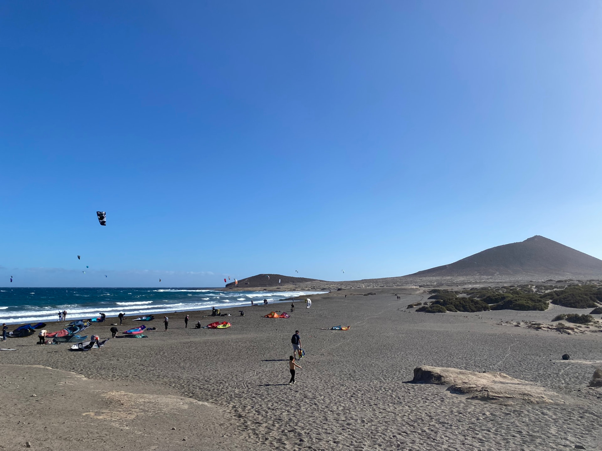 Kitesurfers on a wide volcanic beach beneath a hill photographed by Oskar Olszewski