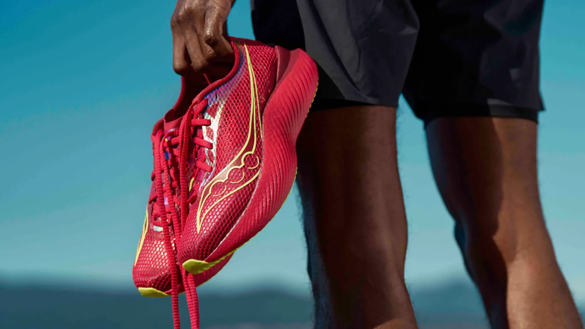 Runner holding a red Saucony Endorphin Pro 3 running shoe against a blue sky